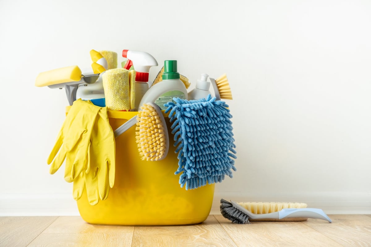 Cepillos, botellas con líquido limpiador, esponjas y guantes de protección en una cubeta de madera